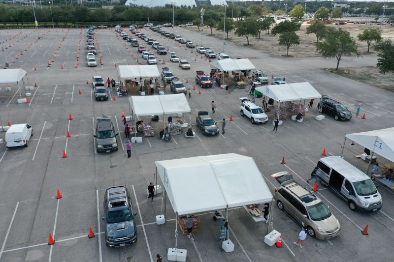 A smiling girl stands in front of a red slide at a park, holding a paper bag.